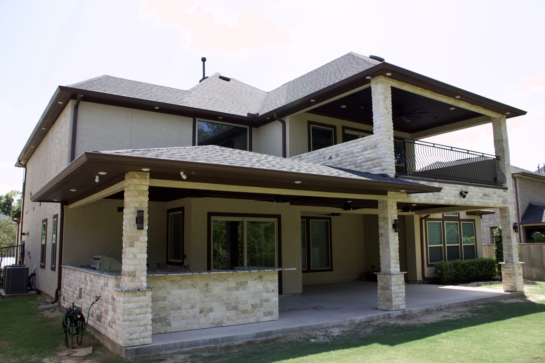 Upper covered patio with wrought-iron railing and stone columns