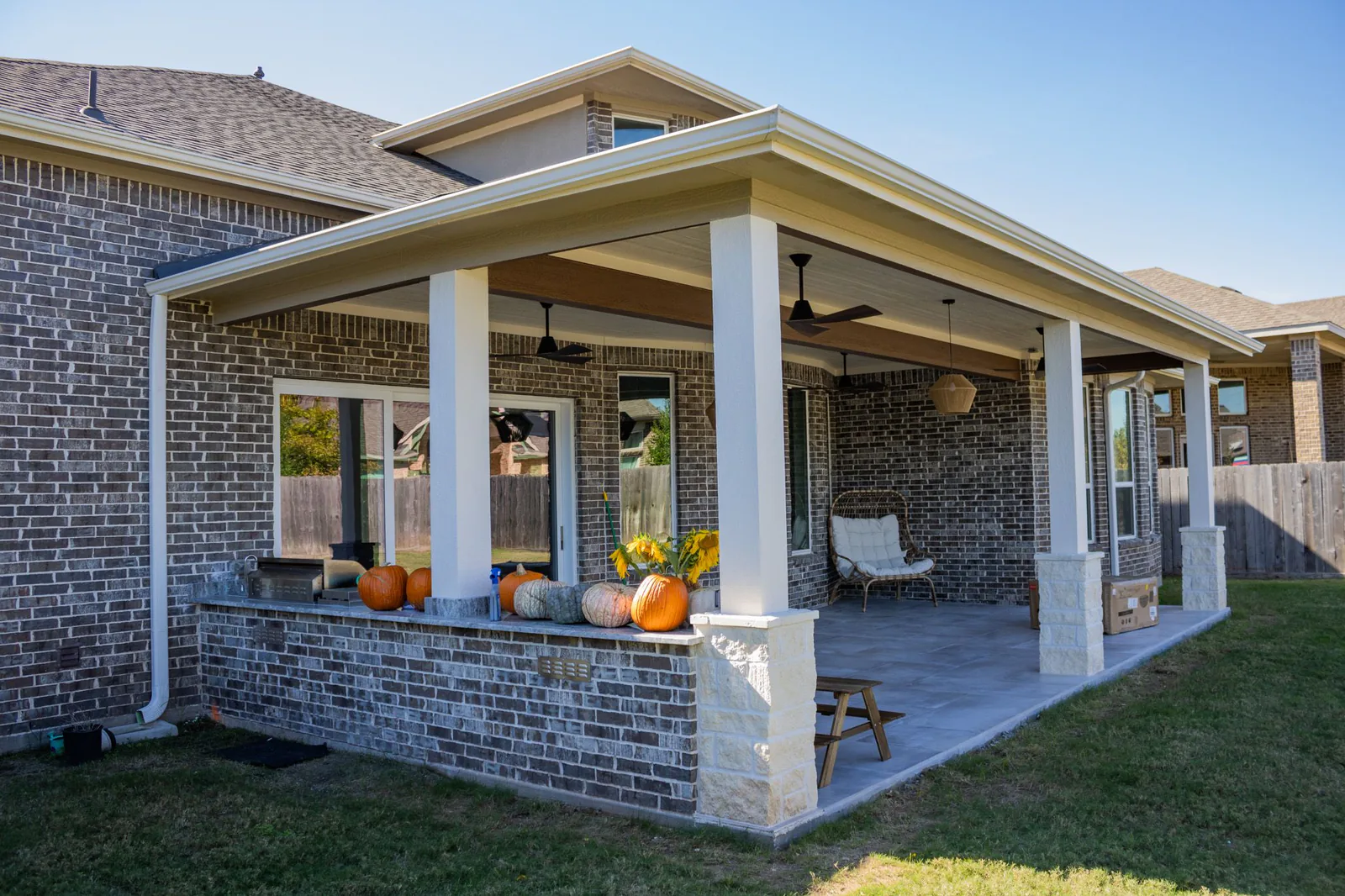 Low-slope patio cover with ceiling fans, brick half wall, and outdoor kitchen