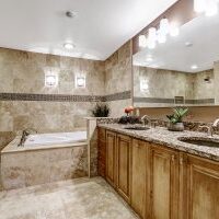 Luxury bathroom interior with tile floor. Bath tub with brown granite tile trim and vanity cabinet with large mirror.