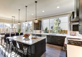 Modern gray kitchen features dark gray flat front cabinets paired with white quartz countertops and a glossy gray linear tile backsplash. Bar style kitchen island with granite counter. Northwest USA
